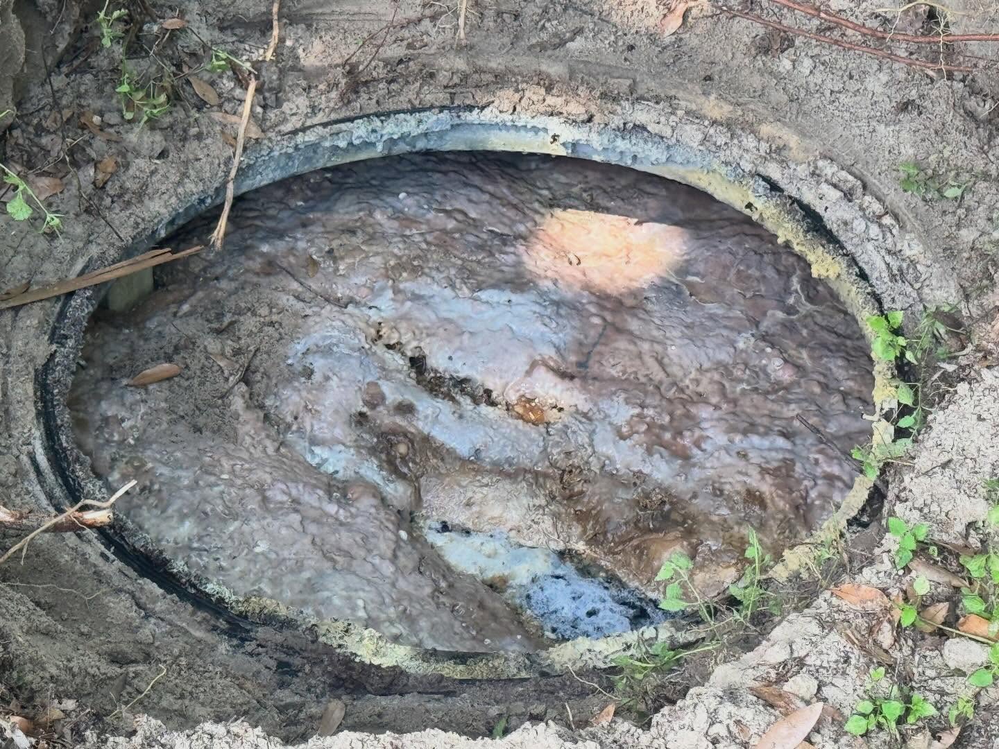 Open septic tank filled with wastewater and accumulated solids, showing a septic system in need of pumping and maintenance.